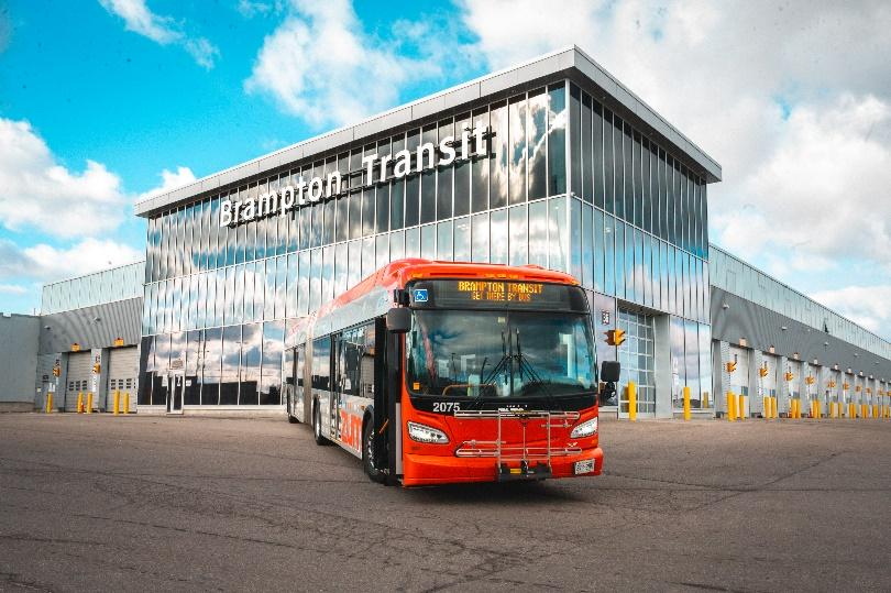 Red Brampton Transit bus parked in front of the modern Brampton Transit facility under a blue sky.