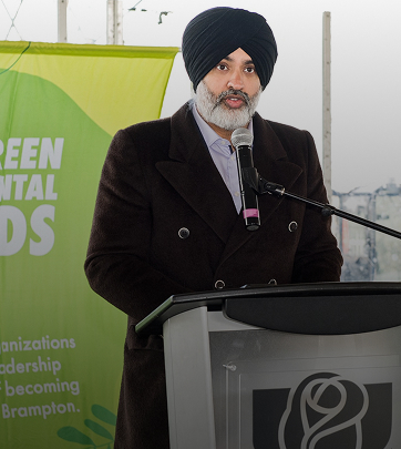 Man speaking at podium about green initiatives with banner in background.